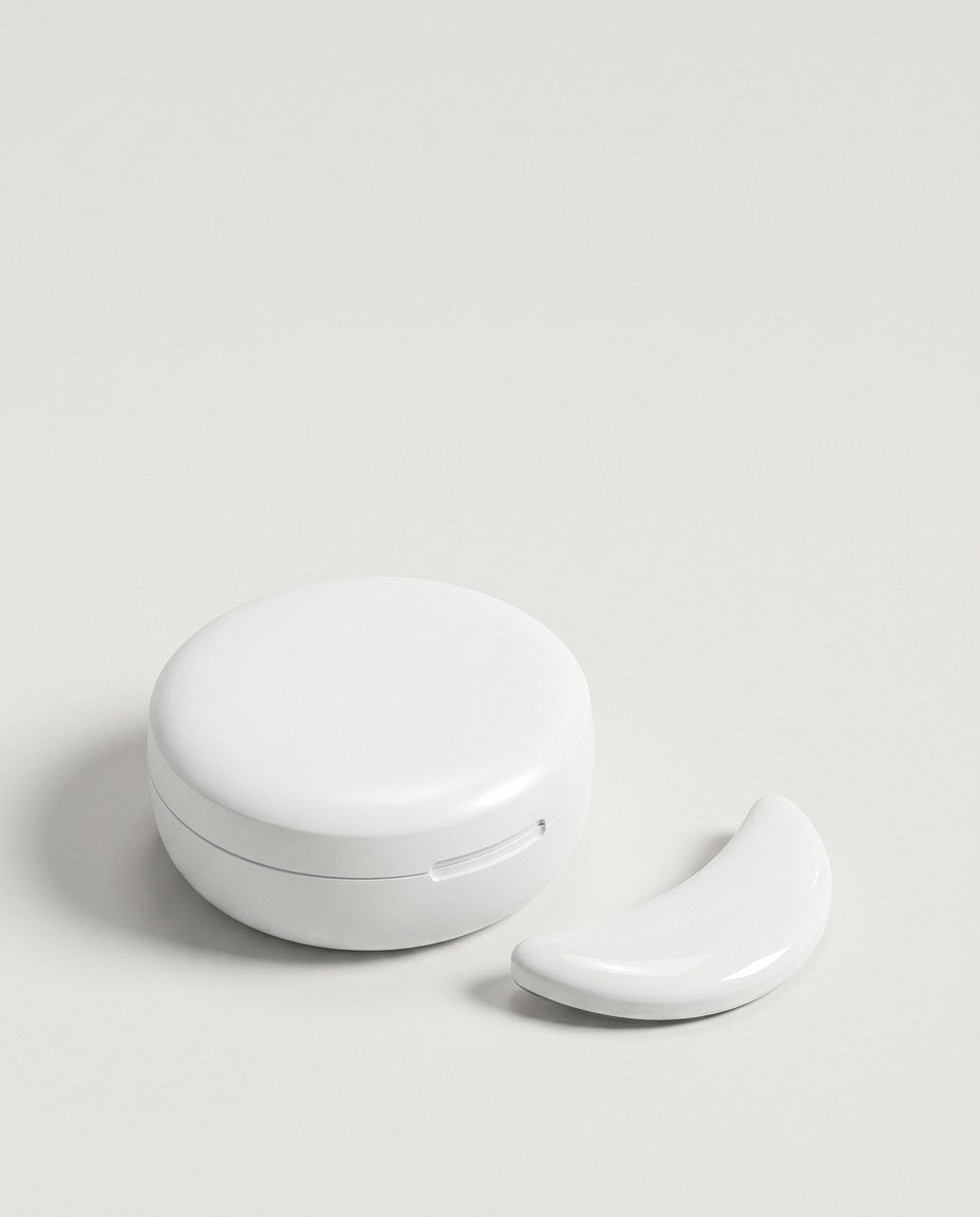 The closed round charging case with one unlit under-eye pad beside it