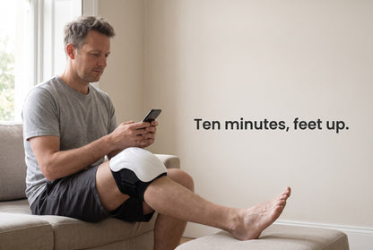 Man sitting on a sofa with the joint massager on his knee, feet up