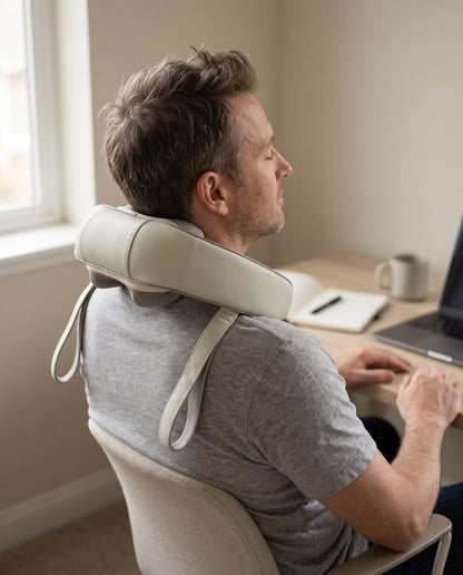 Man leaning back at his desk wearing the neck and shoulder massager, hands on the chair arms